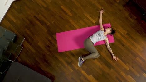 stretching in a lying twisted position, moving from the left to the right side as the woman is lying on her pink yoga mat