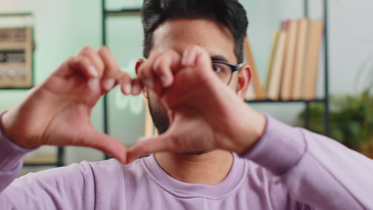 행복한 인디언 남자는 사랑의 상징을 만니다. 카메라에 심장 기호를 보여주고 로맨틱한 감정을 표현합니다.