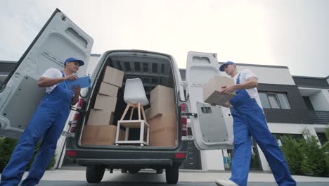 two young workers of removal company are loading boxes and furniture into a minibus