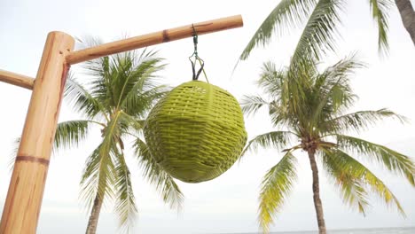 Woven straw decoration hang on bamboo pole with palm trees in background