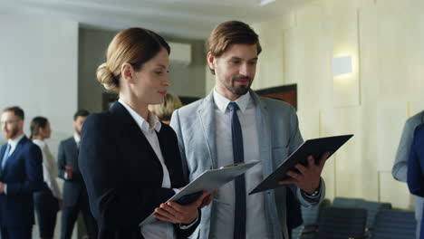 caucasian businesswoman and her male colleague talking and discussing documents in the hall at a meeting