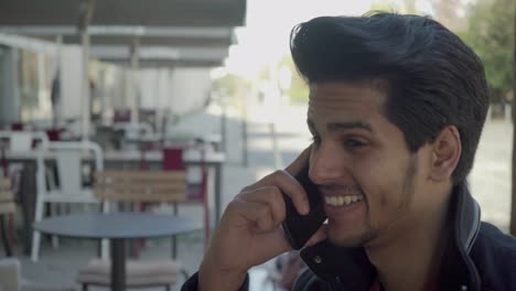 Happy-young-man-talking-by-cell-phone-in-outdoor-cafe