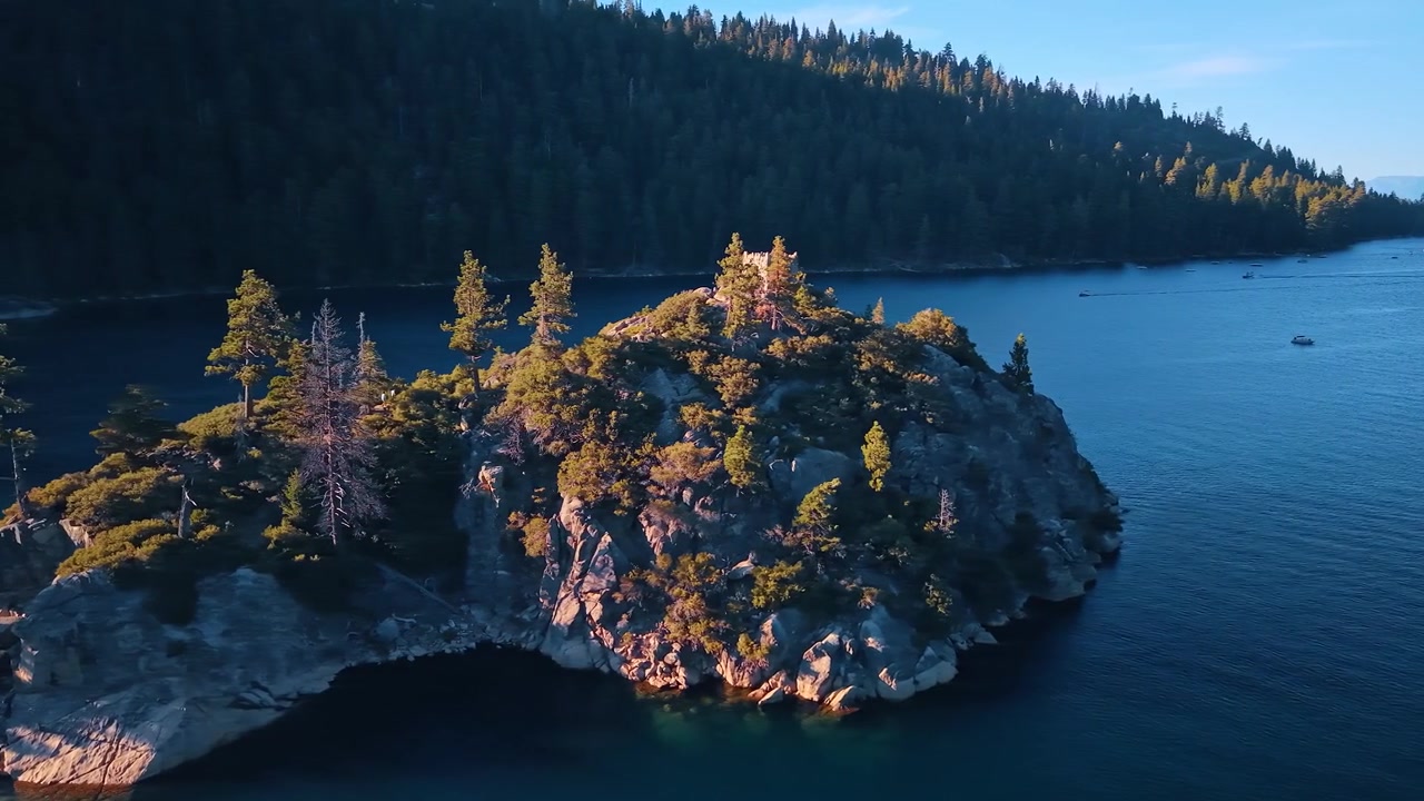 Wooded cliffs of Fannette Island above Emerald Bay. Trees and shrubs cover a granite island, with a small ruin on the summit and forest beyond the water.