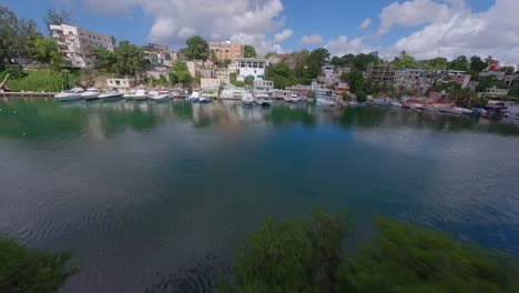 aerial fpv flight above tropical river with parking boats and city of romana in background, dominican republic