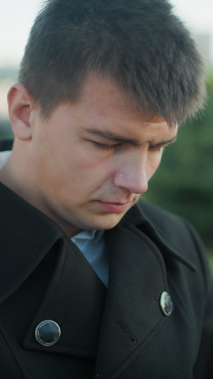 검은색 슈트를 입은 남자가 노트북을 가지고 야외에서 일하고 있으며, 초점을 맞춘 표정, 배경 특징은 주차된 자동차와 도시 건물을 흐릿하게 나타니다.