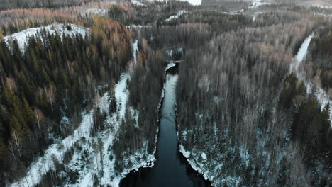 Aéreo,-Decreciente,-Inclinado-Hacia-Arriba,-Disparo-De-Drones,-Bengalas-Solares,-Sobre-Un-Río,-Rodeado-De-Bosque-Sin-Hojas-Y-Primeras-Nevadas-En-El-Suelo,-En-Un-Día-Soleado-De-Invierno,-Cerca-De-Joensuu,-Karelia-Del-Norte,-Finlandia