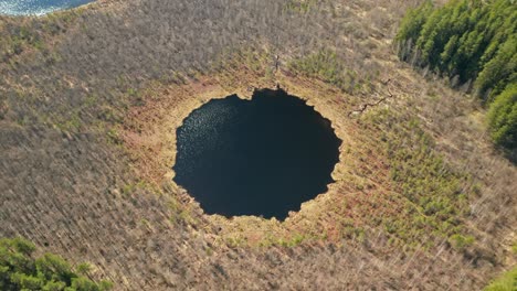 aerial: rotating shot of round deep blue lake in forest