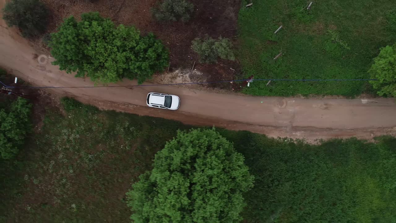 Dron aéreo cenital siguiendo un vehículo blanco en una carretera estrecha entre pinos verdes