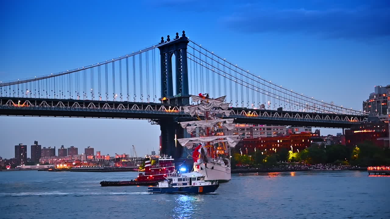 Old-style sheep with white sail near the Manhattan Bridge in New York. Police boat moves nearby. Big Apple in the evening