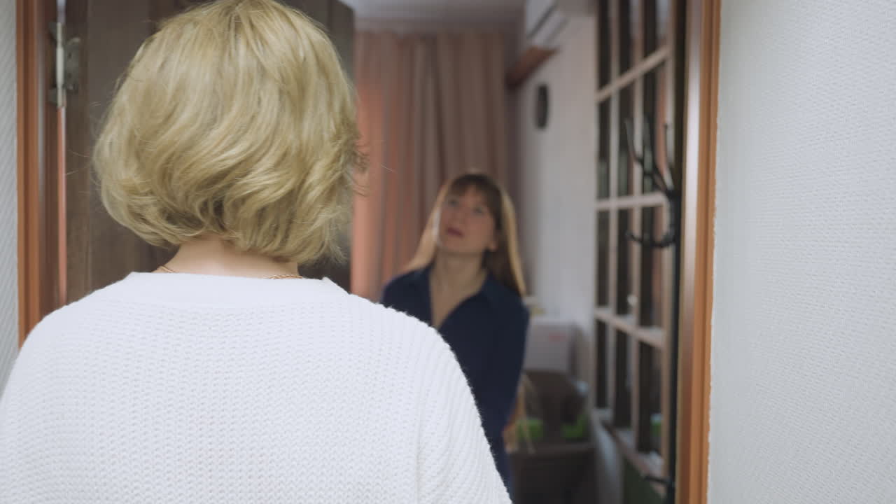 Back view of woman in white sweater knocking on wooden door in quiet hallway as therapist prepares to open door with warm smile, cozy room with sofa and tables visible inside
