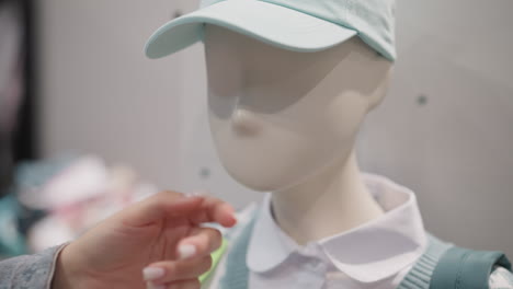 woman touches child mannequin in store closeup. happy customer plays with dummy in blue cap visiting clothes shop. playful buyer at shopping