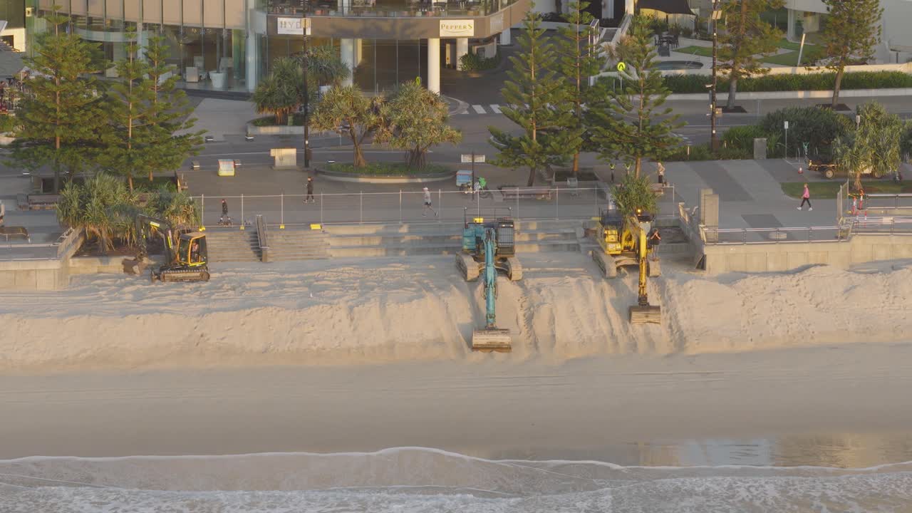 Attrezzature da costruzione e operai riparano la spiaggia a Gold Coast. La luce del primo mattino proietta lunghe ombre sulla sabbia.