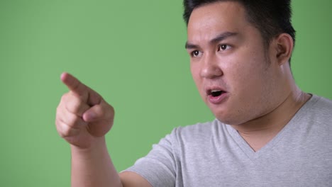 young handsome overweight asian man against green background