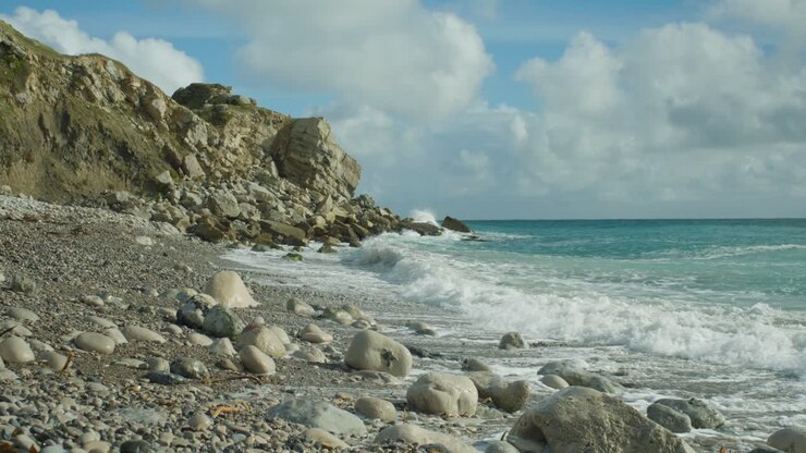 Ripresa cinematografica in slow motion 4K di onde che si infrangono sulle rocce di una spiaggia, a Church Ope, Portland Dorset, in Inghilterra, in una giornata di sole, con scogliere sullo sfondo.