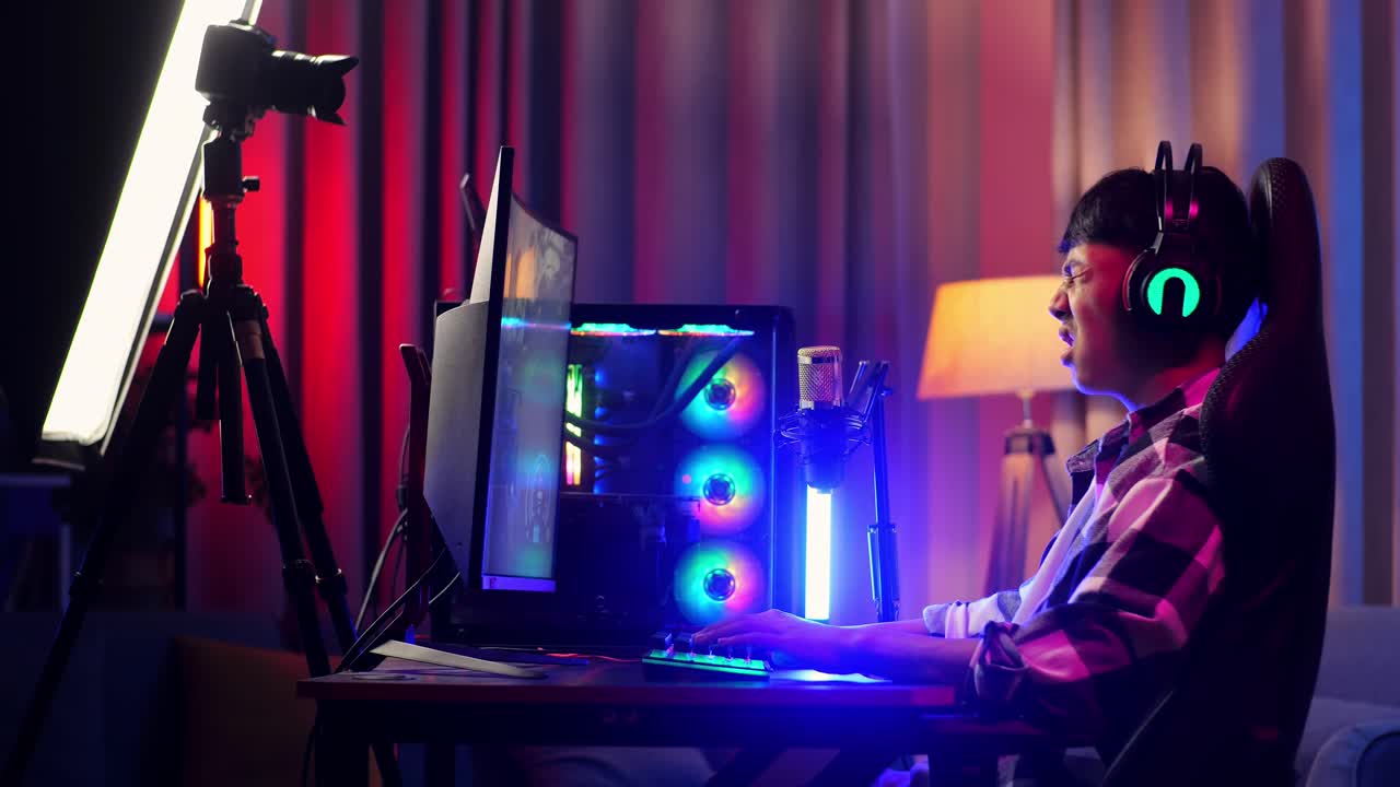 vista lateral de un streamer asiático con dolor de espalda mientras juega un juego a través de la red en una computadora personal. videojuego de transmisión en vivo, escritorio iluminado por luz de tira led rgb