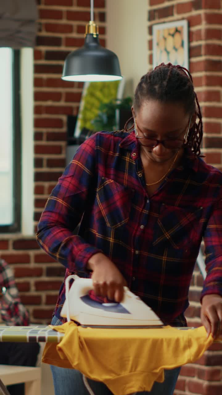 Vertical video: Young modern housewife using heat iron and ironing table