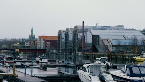camera pans across the port of trondheim, norway, revealing an industrial waterfront framed by a misty, cold day. boats rests quietly at the dock. in the distance, a bus moves across a bridge.