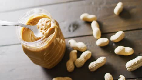 Video-of-close-up-of-peanut-butter-and-peanuts-on-wooden-background