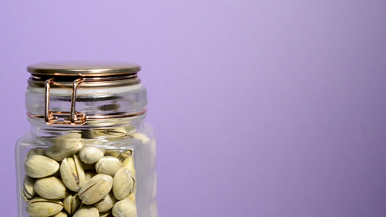 detalle de un tarro de albañil hermético que gira con pistachos sobre un fondo lila neón