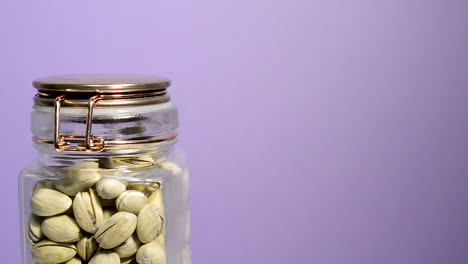 detalle de un tarro de albañil hermético que gira con pistachos sobre un fondo lila neón