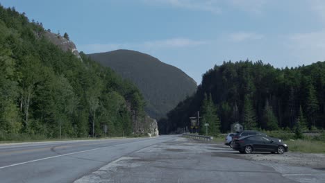 A-wide-angle-shot-of-a-mountain-pass,-where-a-road-is-cut-through-granite-as-mountains-stand-in-the-background