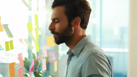 Male-executive-looking-at-sticky-notes-on-glass