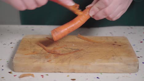 caucasian woman peeling carrot over wooden cutting board, closeup