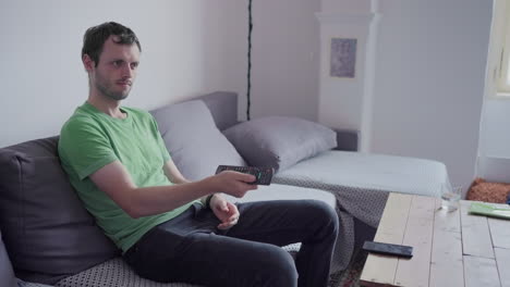 Young-man-with-dark-hair-watching-tv-and-changing-the-channels-with-remote-control