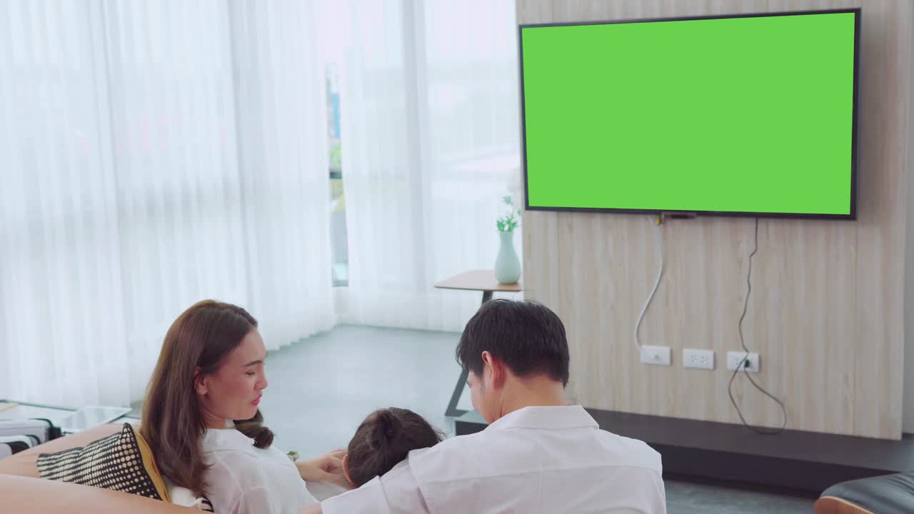 행복한 아시아 가족은 집에서 거실에서 텔레비전을 보고 함께 리티 타임을 보내고, 메시지를 위해 녹색 스크린 모니터로 채널을 전환합니다.