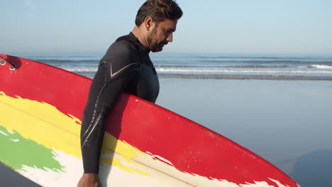 vertical motion of a male surfer with artificial leg walking along beach and holding surfboard under arm