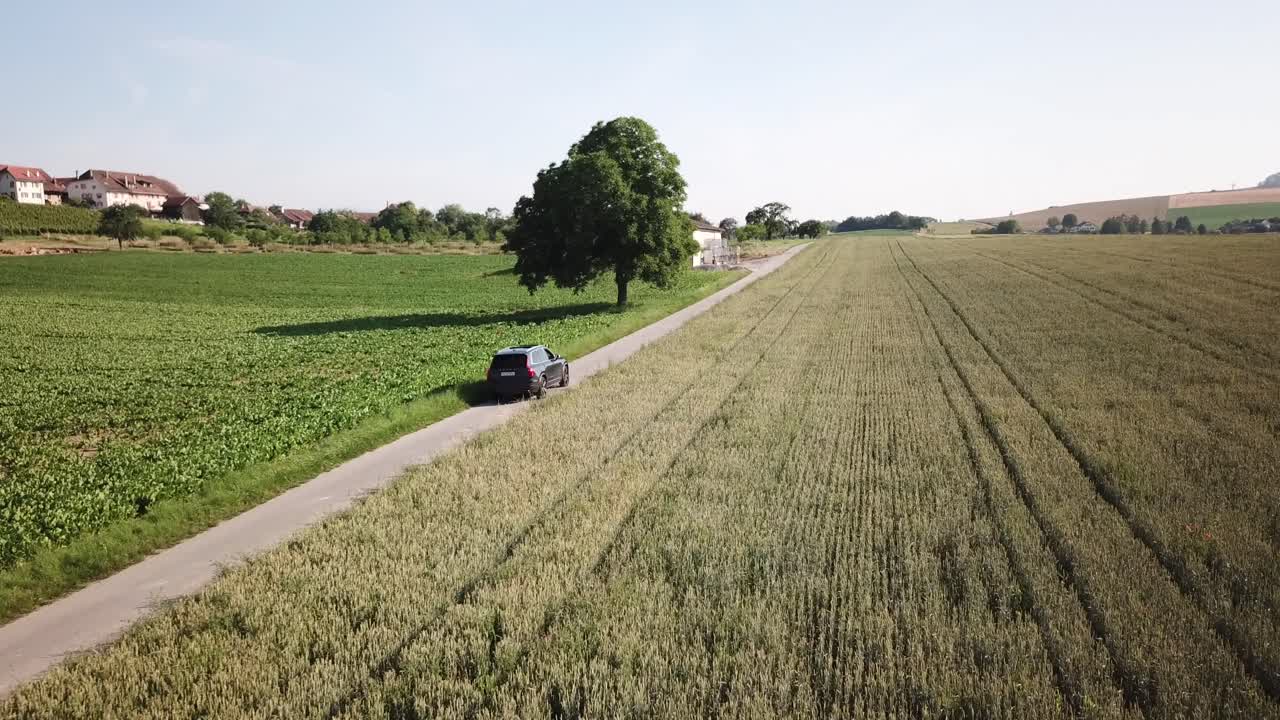 un automóvil volvo xc90 conduce solo en una pequeña carretera rural, rodeado de vastos campos agrícolas, suiza, vaud, toma aérea de drones