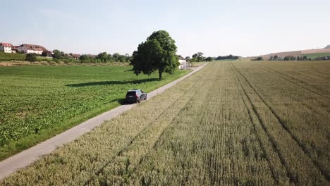 a-volvo-xc90-car-drives-alone-on-a-small-country-road,-surrounded-by-vast-agricultural-fields,-Switzerland,-Vaud,-aerial-drone-shot