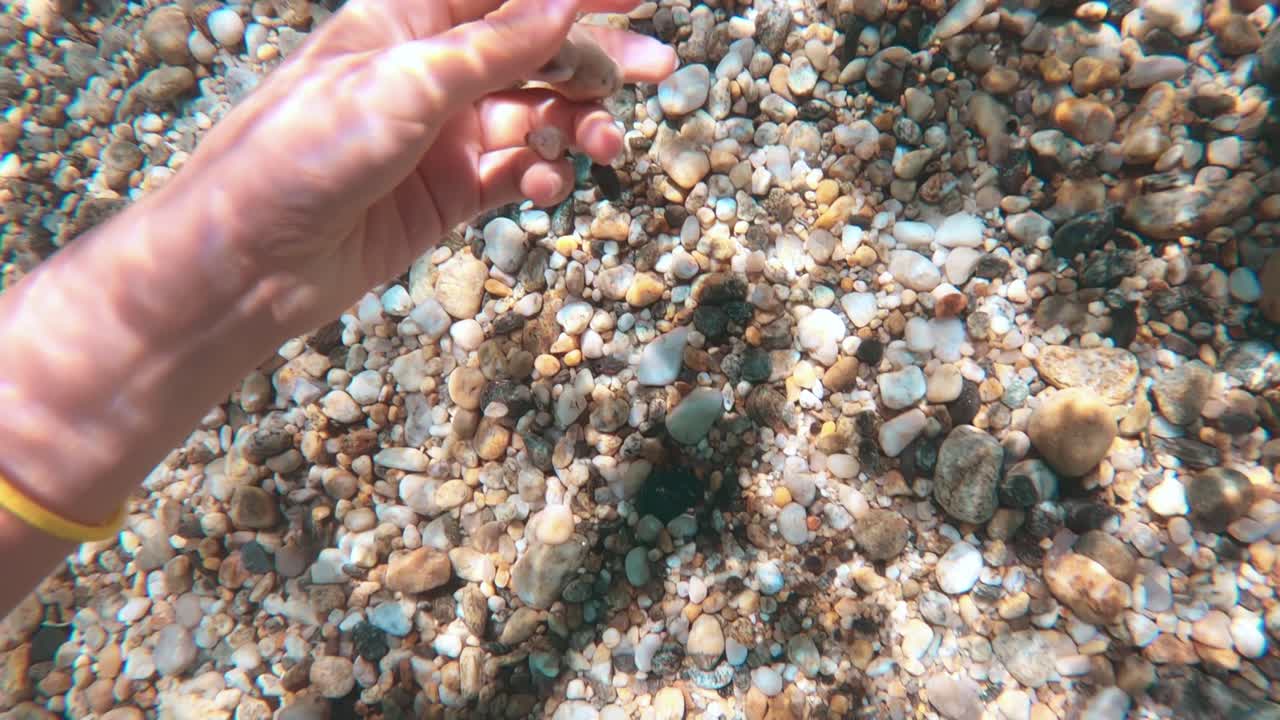 Female hand taking rocks from the bottom of the Aegean sea visible through the clear water, refraction of light. Greece
