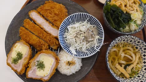 a top-down reveal of complete japanese tonkatsu set meal, featuring crispy original and cheese-filled pork cutlets, rice, shredded cabbage salad, and a bowl of udon noodle soup
