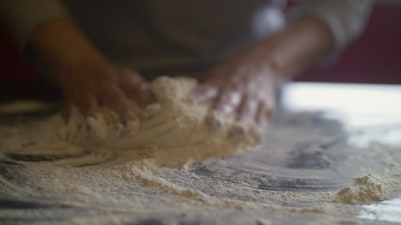 manos de mujer haciendo masa de pizza en una mesa de mármol llena de harina