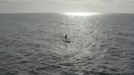 aerial retreats from sup paddle boarder in sun beam on choppy ocean