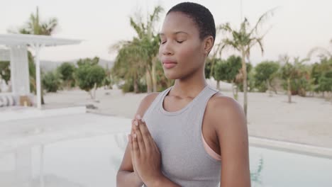 Relaxed-biracial-woman-practicing-yoga,-meditating-on-beach,-slow-motion