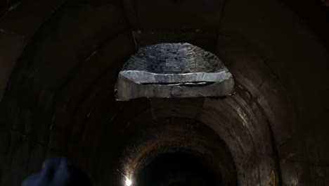 an escape hole in a dark underground tunnel letting in light from above the subterranean concrete bunker