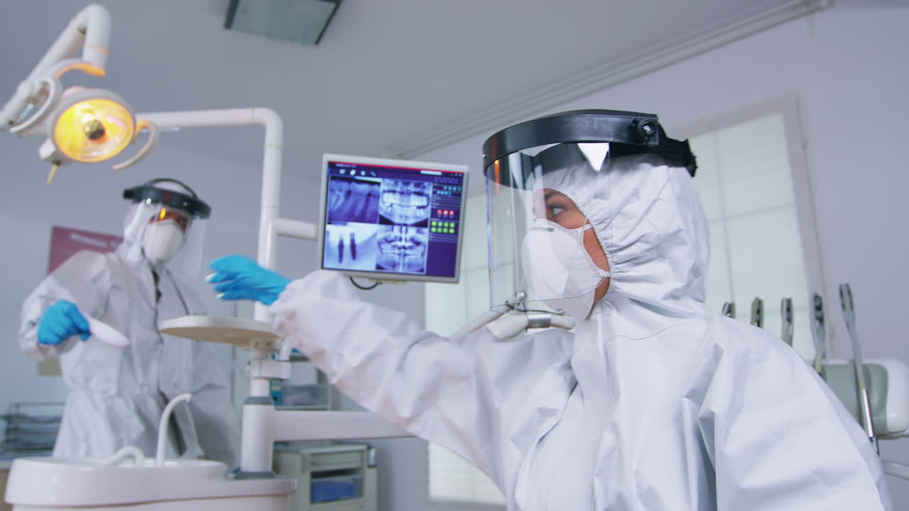 paciente del dentista en traje de ppe midiendo la temperatura de la persona