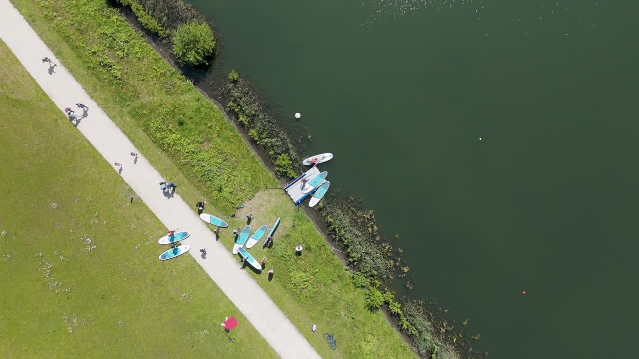 Capture a peaceful aerial view of people preparing kayaks and launching into a serene lake, surrounded by vibrant greenery—perfect for nature and adventure footage.