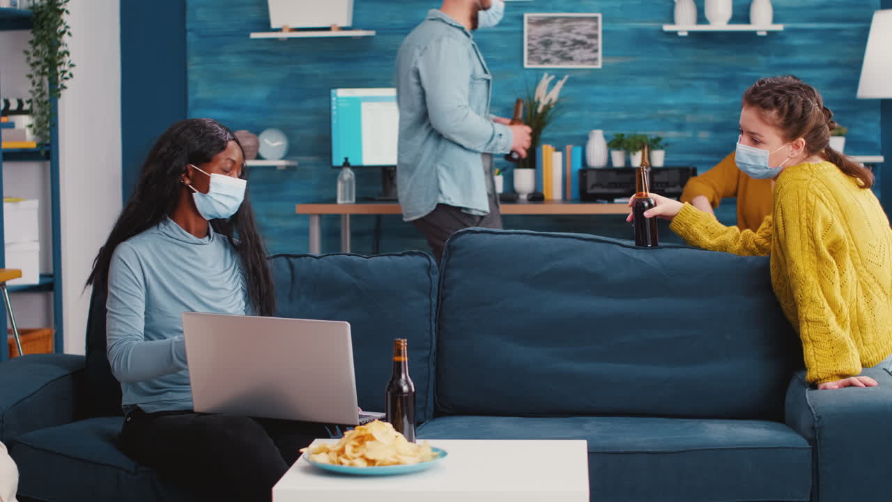 Woman holding beer bottle looking at laptop discussing with friend