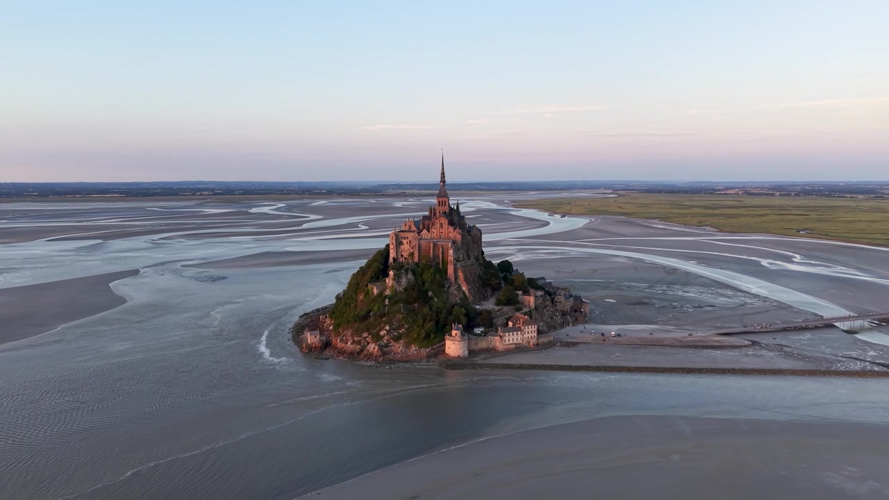 Cinematic drone orbit around Mont Saint-Michel Abbey at sunset showcasing the island monastery and expansive tidal flats in Normandy, France