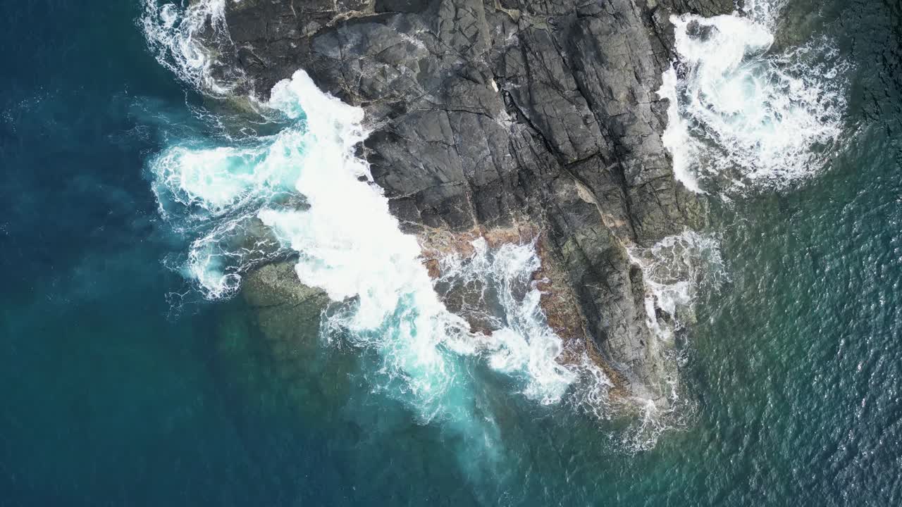 Suggestiva vista aerea dall'alto di onde oceaniche turchesi che si infrangono contro le rocce costiere