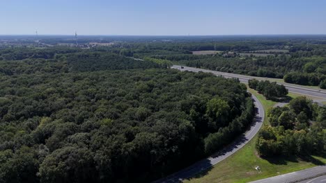 american highway in suburb with green forest trees and blue sky. aerial rising wide shot. modern interstate roads in rural area of wisconsin. cars and trucks on asphalt expressway