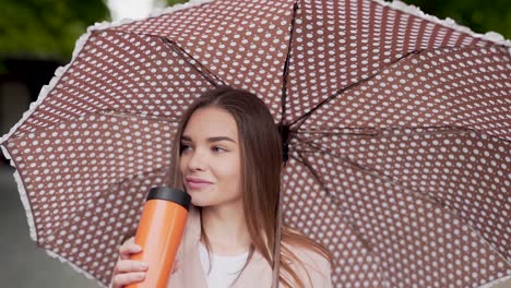 beautiful girl drinks a drink from a thermos holding an umbrella