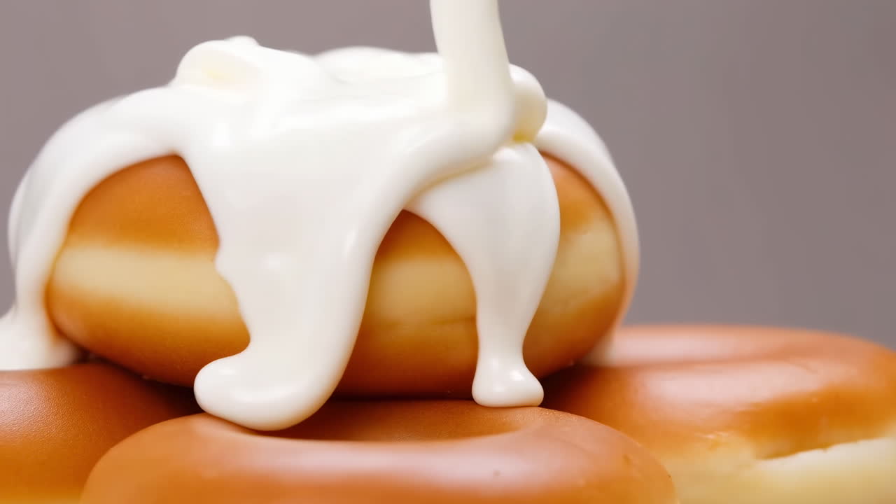 Pila de donas calientes con glaseado vertiéndose, primer plano de estudio de glaseado cremoso en cascada sobre rosquillas doradas, espeso.