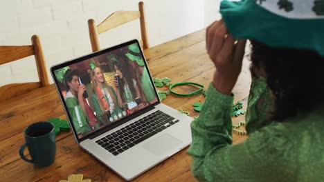 Mixed-race-woman-at-home-using-laptop-making-video-call-on-st-patrick's-day