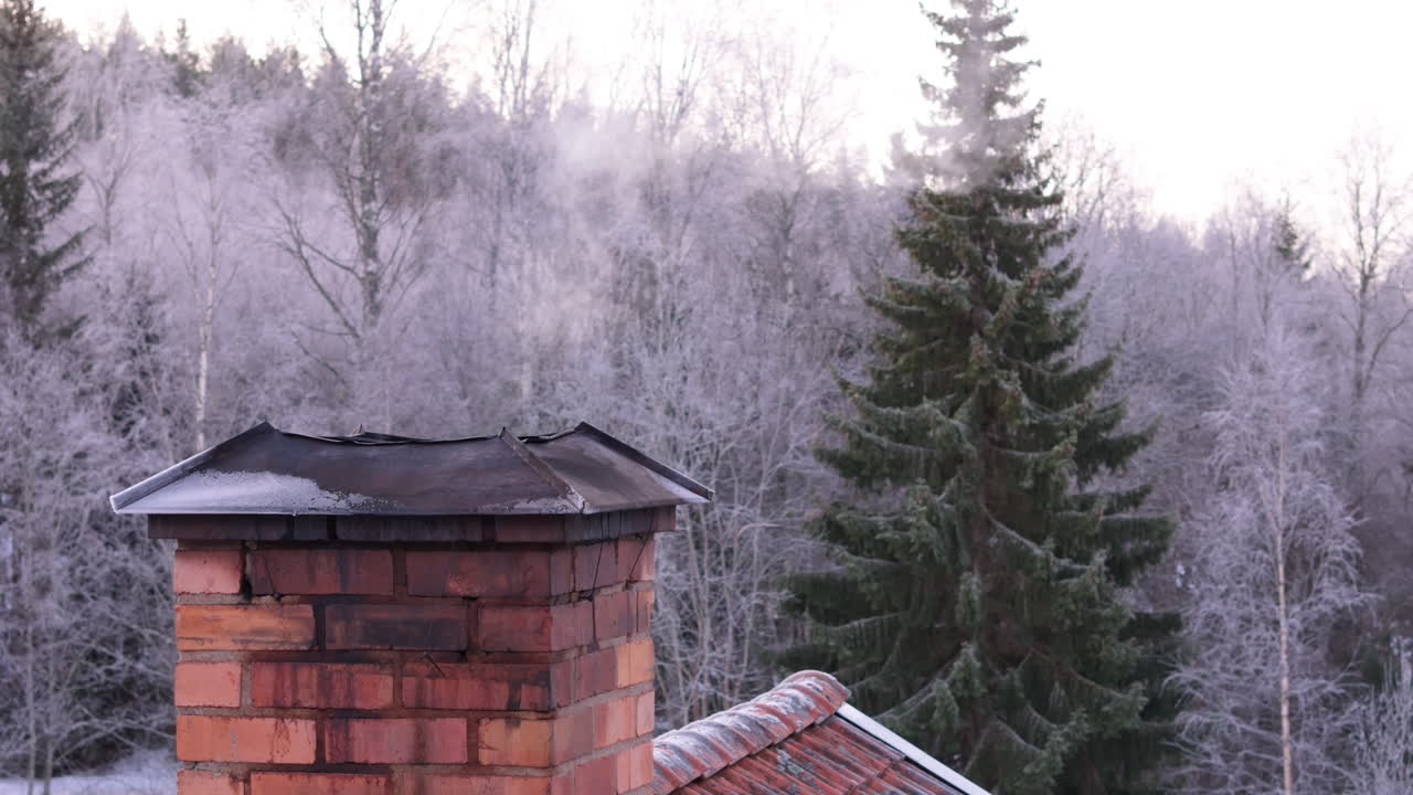 Smoke escapes brick chimney of house in the woods on crisp winter day. Aerial