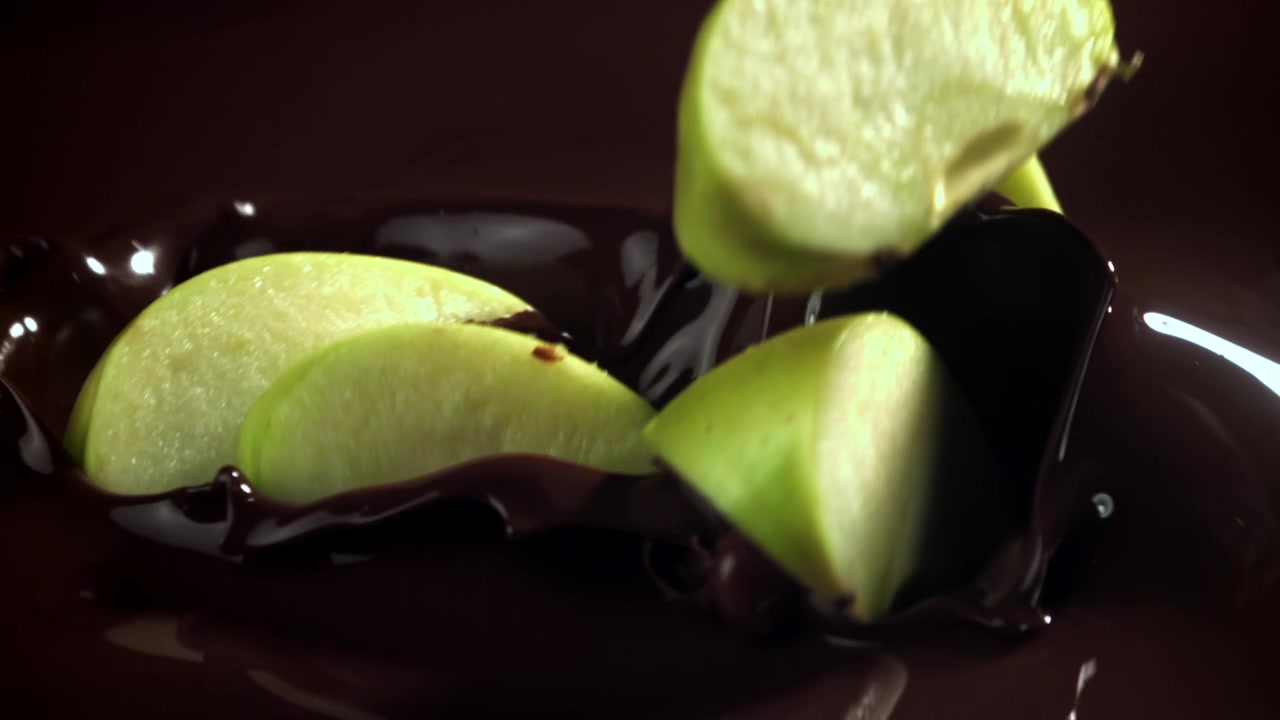 Fette di mela verde che cadono nel cioccolato fondente fuso al rallentatore