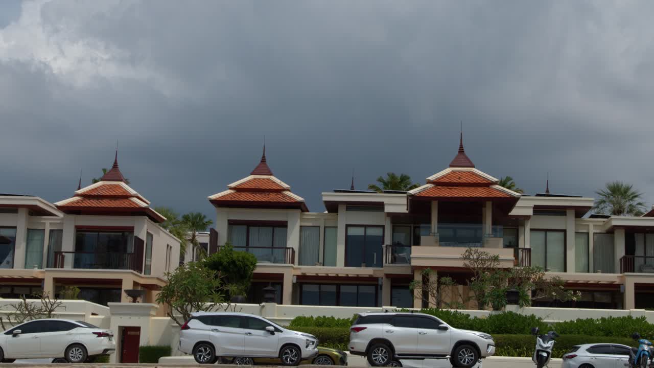 Statisk vidvinkelbillede af luksuriøse Phuket-villaer med traditionel arkitektur under en dramatisk skyet himmel.